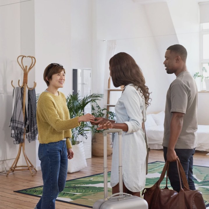 A host welcoming two guests with luggage